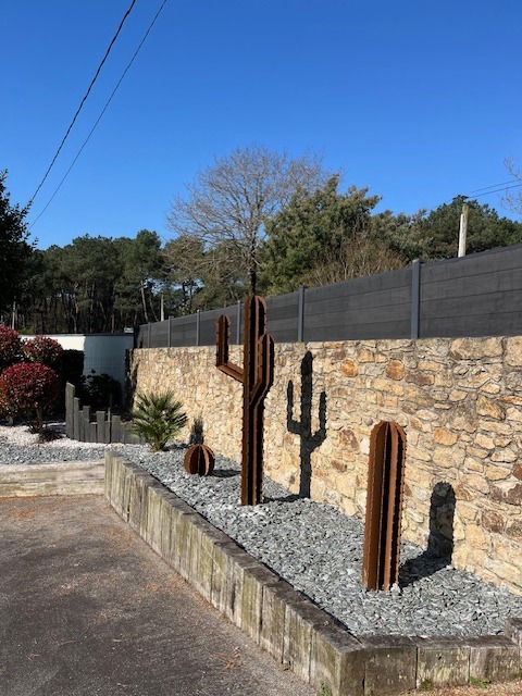 Trois cactus décoratifs en corten intégrés dans un massif paysager